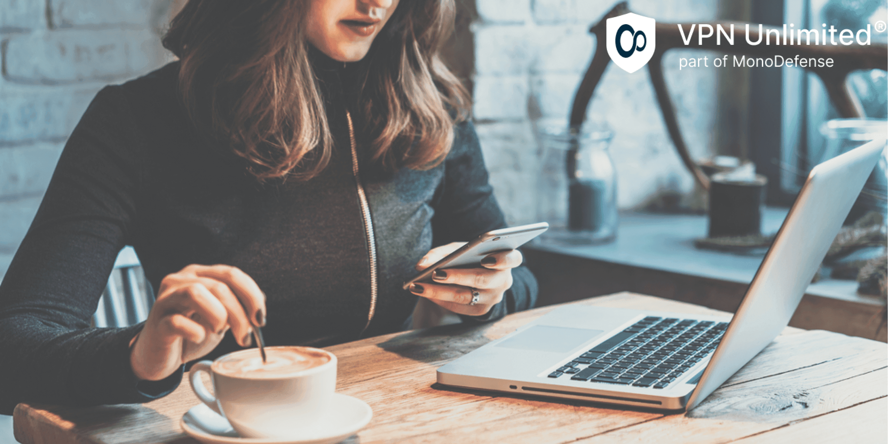 Young woman sitting in coffee shop at wooden table, drinking coffee and using smartphone, concept of cyber threats on public WiFi